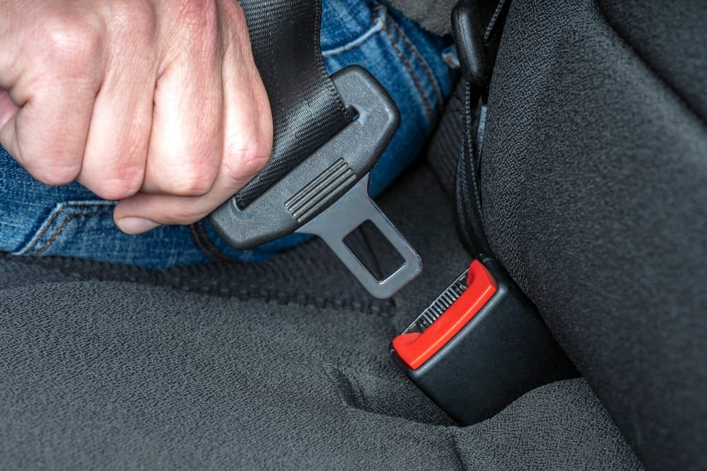 A close up of a man's hand buckling a seatbelt in a vehicle.